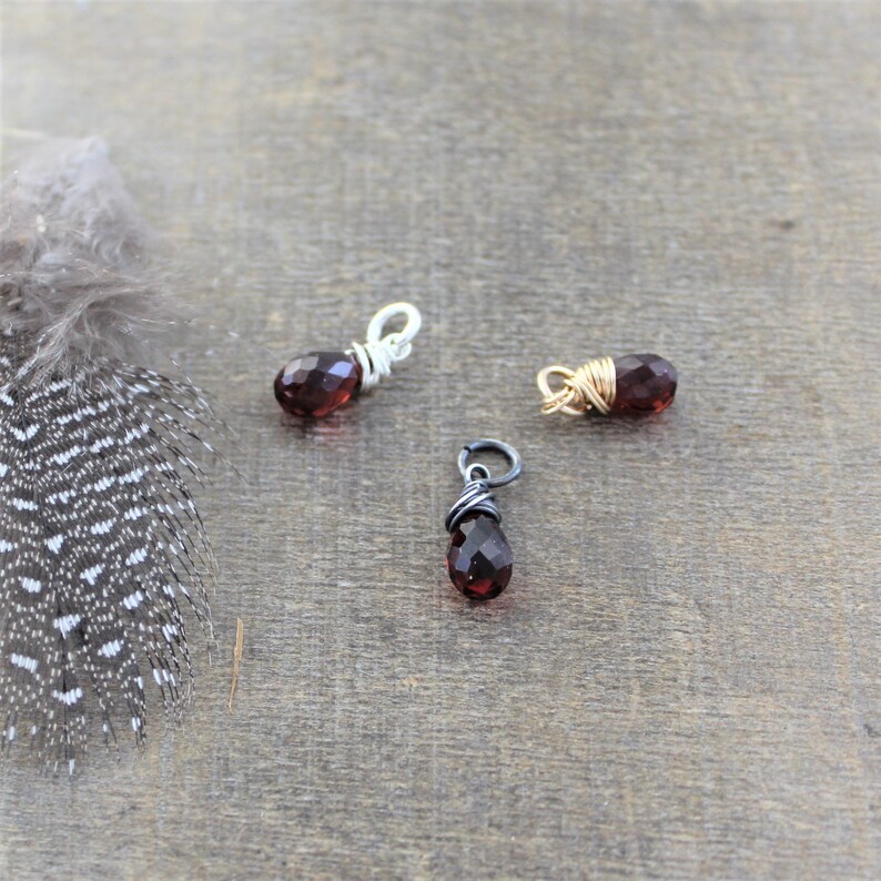 May include: Three small teardrop-shaped red gemstone pendants wrapped in silver, gold, and black wire.