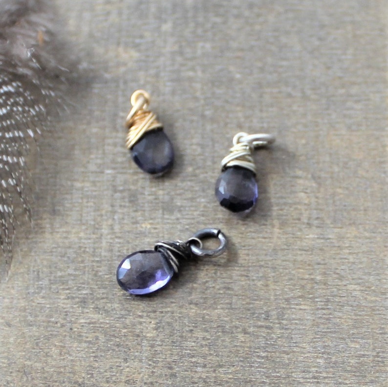 K&ouml;nnte beinhalten: Drei drahtgewickelte Edelstein-Anh&auml;nger mit einem violetten Amethyst-Stein. Die Anh&auml;nger sind aus Gold-, Silber- und schwarzem Draht gefertigt.