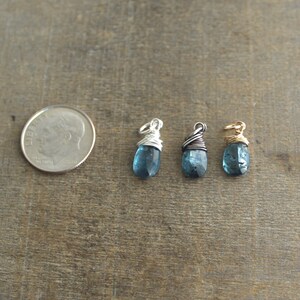May include: Three teardrop-shaped blue topaz pendants wrapped in silver, gold, and black wire.