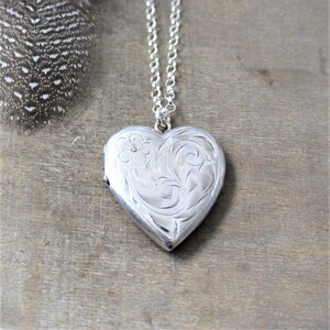 May include: A silver heart-shaped locket necklace with a delicate floral design. The locket has a hinged opening and is perfect for holding a small photo or memento.