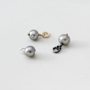 May include: Three silver, gold, and black pearl charms with a loop for attaching to a necklace or bracelet.