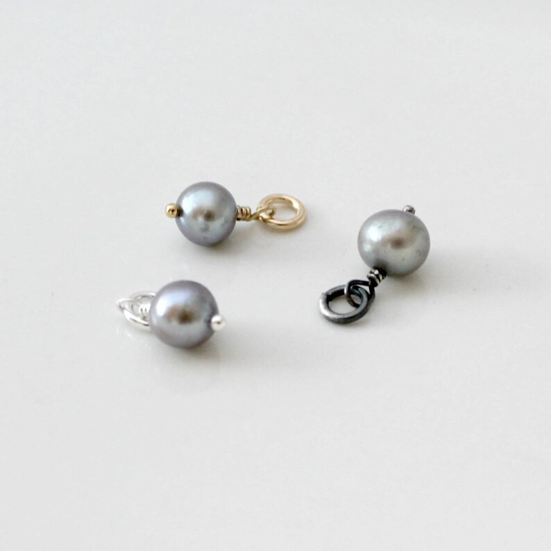 May include: Three silver, gold, and black pearl charms with a loop for attaching to a necklace or bracelet.