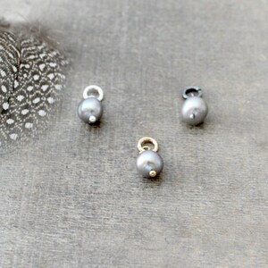 May include: Three silver, gold, and black pearl charms with a loop for attaching to a necklace or bracelet.