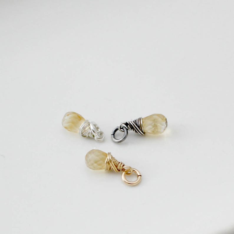 May include: Three small teardrop-shaped gemstone charms with wire wrapping. The charms are made with a light yellow gemstone and silver or gold wire.