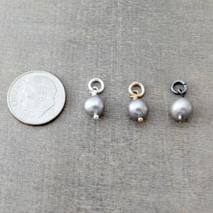 May include: Three silver, gold, and black pearl charms with jump rings. The charms are about the size of a dime.
