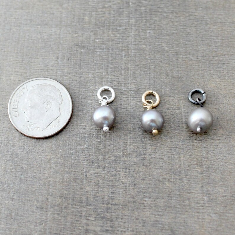 May include: Three silver, gold, and black pearl charms with jump rings. The charms are about the size of a dime.