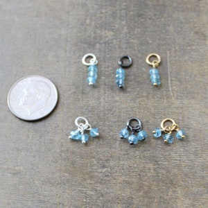 May include: Six different charms featuring blue topaz gemstones. The charms are made with silver, gold, and black metal.