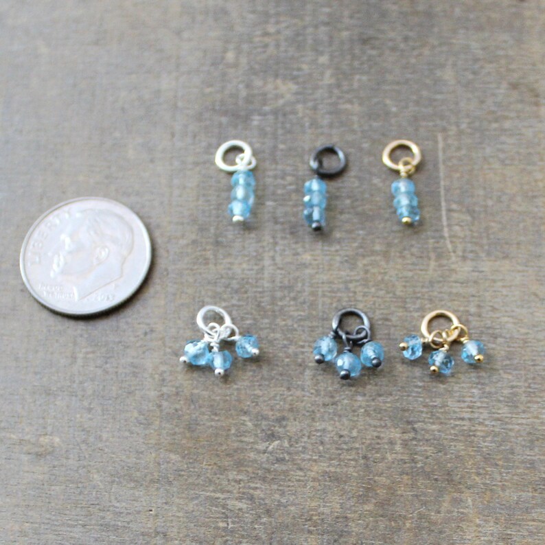 May include: Six different charms featuring blue topaz gemstones. The charms are made with silver, gold, and black metal.