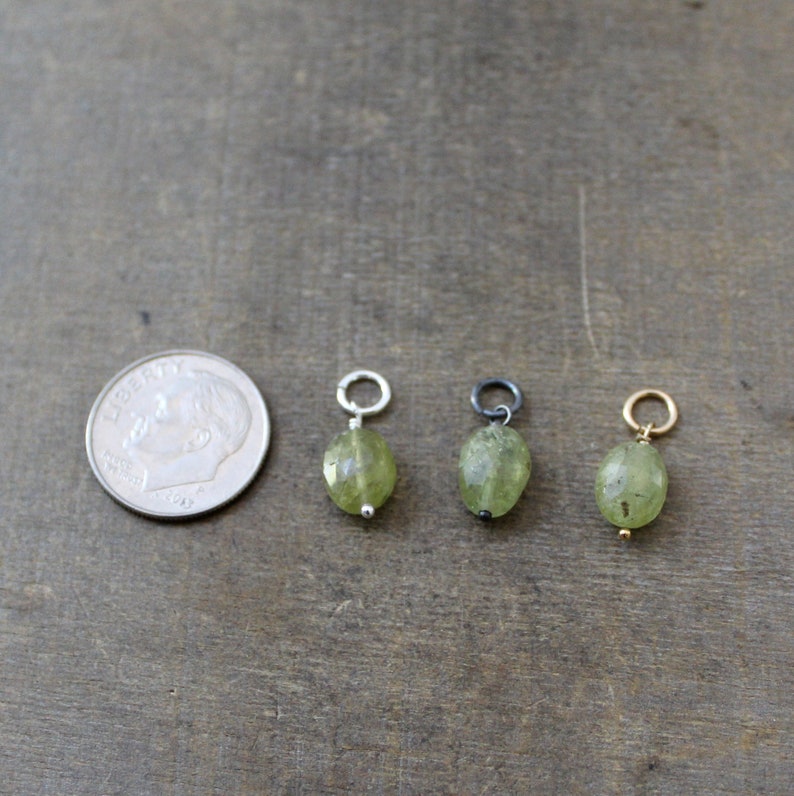 May include: Three green gemstone pendants with different colored metal loops. The pendants are oval shaped and have a faceted finish. The loops are silver, black, and gold.