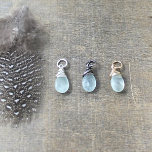 Peut inclure: Trois pendentifs en forme de larme en pierre d'aigue-marine enveloppés de fil. Les pendentifs sont argentés, noirs et dorés.