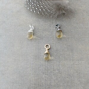 May include: Three wire-wrapped teardrop-shaped pendants with a gold, silver, and black wire. The pendants are made with a light yellow gemstone.