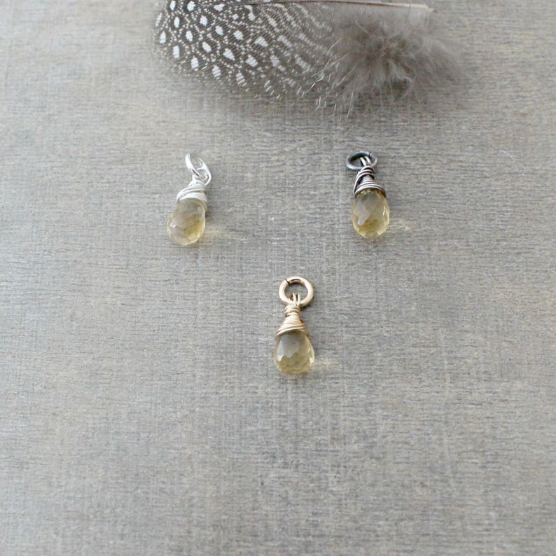 May include: Three wire-wrapped teardrop-shaped pendants with a gold, silver, and black wire. The pendants are made with a light yellow gemstone.