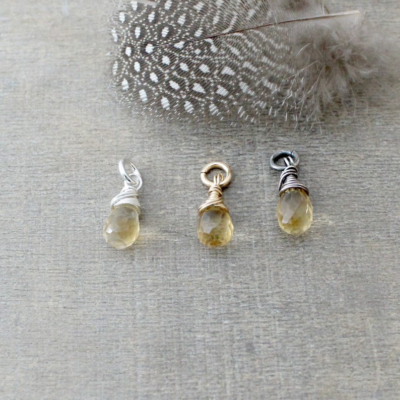May include: Three wire-wrapped teardrop-shaped pendants with a light yellow gemstone. The pendants are made with silver, gold, and black wire.