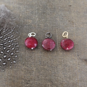 May include: Three red gemstone pendants with different metal settings. The pendants are round and have a faceted finish. The metal settings are silver, black, and gold.