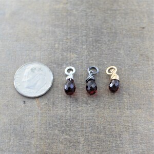 May include: Three small, teardrop-shaped red gemstone pendants with wire wraps. The pendants are shown next to a US dime for size comparison.