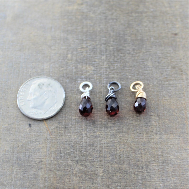 May include: Three small, teardrop-shaped red gemstone pendants with wire wraps. The pendants are shown next to a US dime for size comparison.