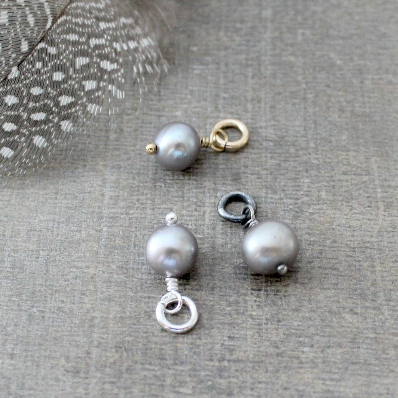 May include: Three gray pearl charms with different metal findings. The charms are on a gray surface.