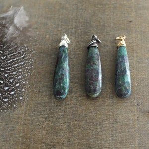 May include: Three green gemstone pendants with silver and gold wire wrapping. The gemstones are a dark green with red flecks.