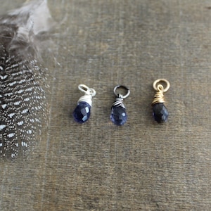 May include: Three wire-wrapped gemstone pendants, each with a different metal finish: silver, gunmetal, and gold. The gemstones are a deep purple color.