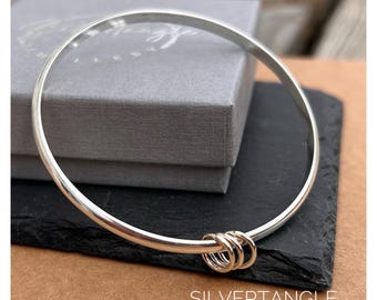 Brazalete redondo de plata con sello de garantía y tres anillos.