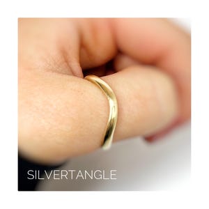 Wavy gold ring worn on a thumb close up image