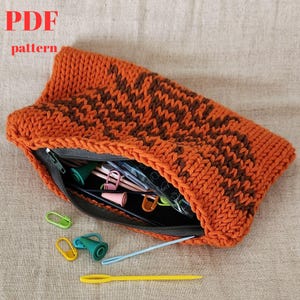 May include: A knitted orange and brown pouch with a zipper closure. The pouch is open and filled with various knitting supplies, including needles, stitch markers, and a plastic bag.