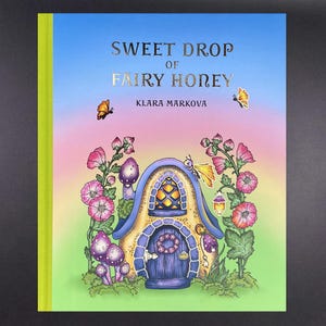 May include: A hardcover book titled Sweet Drop of Fairy Honey by Klara Markova. The cover features a colorful illustration of a small house with a blue roof, surrounded by pink flowers, purple mushrooms, and two butterflies against a gradient sky.