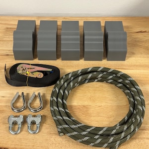 May include: An assortment of gray blocks, metal hardware, a black strap with a ratchet, and a green and white rope are arranged on a wooden surface. The blocks are rectangular with a curved top. The rope is coiled.