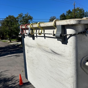 Könnte beinhalten: Ein weißer, rechteckiger Behälter mit einem Seil, das an der Oberseite befestigt ist. Es sind fünf Haken am Behälter befestigt, vier sind gelb und einer ist rot.