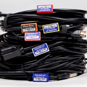 May include: A stack of black cables with various connectors, labeled with blue, red, orange, and yellow stickers. The stickers have the text "SQUARE AV" and a phone number. One sticker has the text "Oliver Bros." and a phone number.