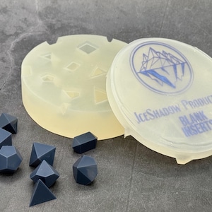 May include: A clear silicone mold with multiple geometric shapes for making dice. The mold is labeled "IceShadow Productions Blank Inserts".  There are several dark gray dice on a gray surface.