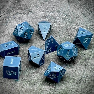 Op de afbeelding: Een set van tien blauwe polyhedrische dobbelstenen met witte nummers. De dobbelstenen zijn in verschillende vormen en maten, waaronder een d4, d6, d8, d10, d%, d12 en d20.