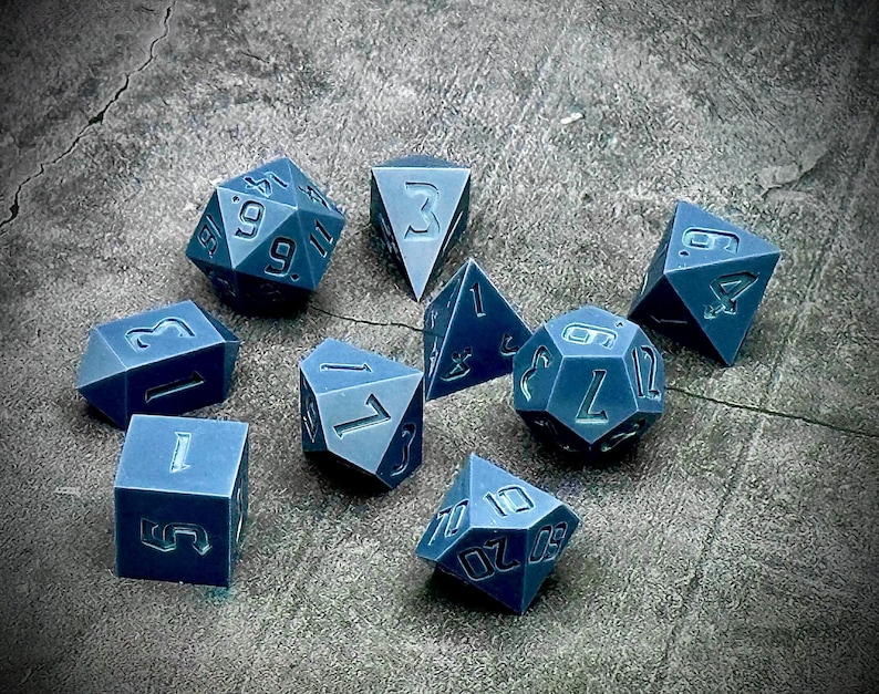 Op de afbeelding: Een set van tien blauwe polyhedrische dobbelstenen met witte nummers. De dobbelstenen zijn in verschillende vormen en maten, waaronder een d4, d6, d8, d10, d%, d12 en d20.