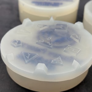 Op de afbeelding: Een transparante siliconen mal met een blauw swirl-ontwerp. De mal is rond en heeft een verhoogde rand. De mal is ontworpen om dobbelstenen te maken met verschillende nummers op elke zijde.