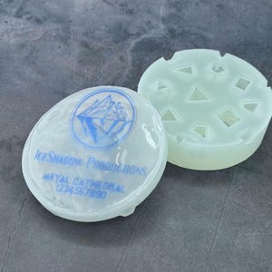 Op de afbeelding: Twee doorschijnende ronde witte mallen. E&eacute;n mal heeft een logo met de tekst "Ice Shadow Productions" en "Metal Cathedral 1774 567 890". De andere mal heeft een patroon van driehoeken en vierkanten.