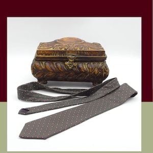 May include: A dark brown rectangular box with an ornate, carved leaf-like texture and a central metal latch, positioned behind a dark brown necktie featuring a repeating pattern of small, light-colored dots. The text 80s Hanover Street is visible.