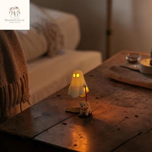 May include: A novelty ghost lamp with a small dog figurine. The lamp has a white ghost with yellow eyes and a red stick. The dog is white with a red collar. The lamp is on a wooden table.