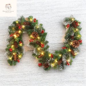 Puede incluir: Una guirnalda navideña en forma de U, adornada con agujas de pino verdes, bayas rojas y piñas. La guirnalda está iluminada con luces de hadas blancas cálidas, creando un ambiente festivo. Ideal para decorar una puerta o una chimenea.