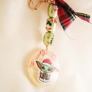 Peut inclure: Un porte-cl&eacute;s de No&euml;l vert et rouge avec un bonhomme de neige, des cannes en sucre et un petit personnage vert portant un chapeau de P&egrave;re No&euml;l. Le porte-cl&eacute;s est attach&eacute; &agrave; un anneau en forme de c&oelig;ur dor&eacute;.