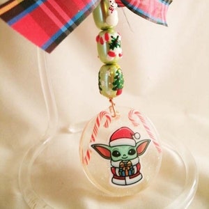 Peut inclure: Une d&eacute;coration de No&euml;l repr&eacute;sentant un personnage vert portant un bonnet de P&egrave;re No&euml;l et tenant un cadeau. La d&eacute;coration est transparente et a une finition scintillante. Le personnage est entour&eacute; de cannes en sucre.