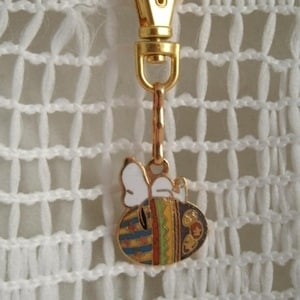 May include: A gold-colored keychain featuring a bee with white wings and a colorful, striped body. The bee is attached to a gold-colored spring clasp.
