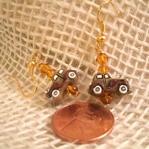 May include: A pair of gold earrings with amber beads and miniature brown cars. The cars have white wheels and details.