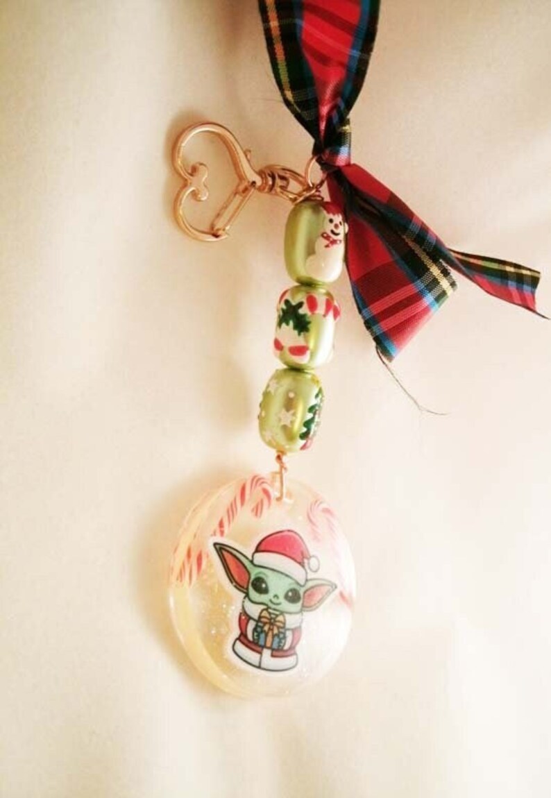 Peut inclure: Un porte-cl&eacute;s de No&euml;l vert et rouge avec un bonhomme de neige, des cannes en sucre et un petit personnage vert portant un chapeau de P&egrave;re No&euml;l. Le porte-cl&eacute;s est attach&eacute; &agrave; un anneau en forme de c&oelig;ur dor&eacute;.