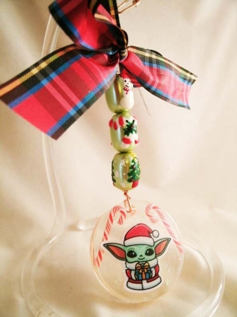 Peut inclure: Une d&eacute;coration de No&euml;l repr&eacute;sentant un personnage vert portant un bonnet de P&egrave;re No&euml;l et tenant un cadeau. La d&eacute;coration est transparente et a une finition scintillante. Le personnage est entour&eacute; de cannes en sucre.
