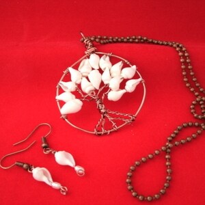 May include: A white seashell tree of life necklace with matching earrings. The necklace has a brown chain and the earrings have silver hooks.