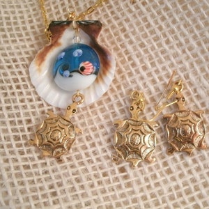 May include: Gold turtle necklace and earrings set with a blue and white glass sea turtle pendant inside a seashell.