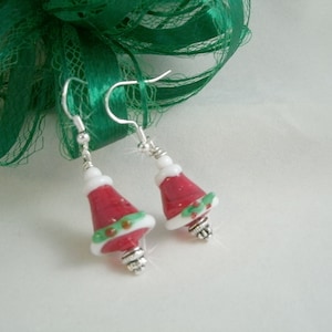 May include: A pair of silver dangle earrings with red and white glass beads shaped like Christmas trees. The beads have green holly accents.