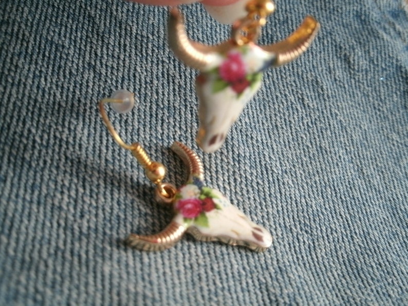 May include: A pair of gold tone earrings with a floral design. The earrings are shaped like a bull's head.