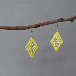 May include: A pair of yellow and white beaded earrings with a diamond shape hanging from a branch.