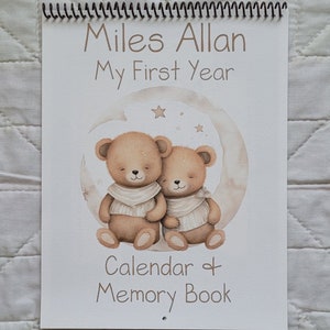 May include: A white spiral bound calendar and memory book with a brown teddy bear illustration. The book has the text "Miles Allan My First Year Calendar & Memory Book" on the cover.